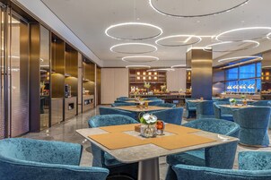A modern restaurant with blue velvet chairs, round tables, and a bar area with wooden cabinets and decorative plants.