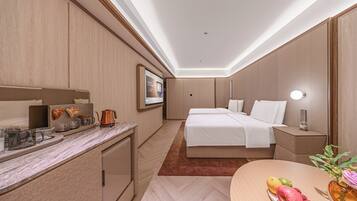 A hotel room with a bed, bedside table, and a desk with a kettle.