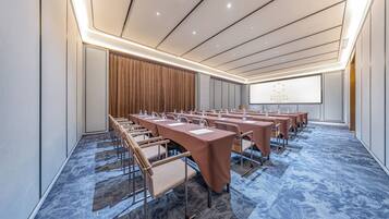 A conference room with rows of tables and chairs, a projector screen, and a carpeted floor.