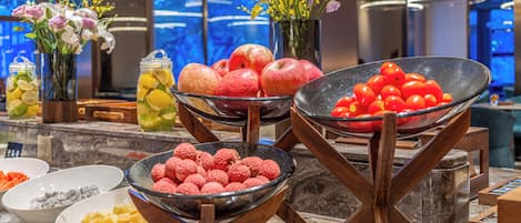A buffet setup with various fruits and vegetables, including apples, tomatoes, and raspberries, arranged on a marble countertop.