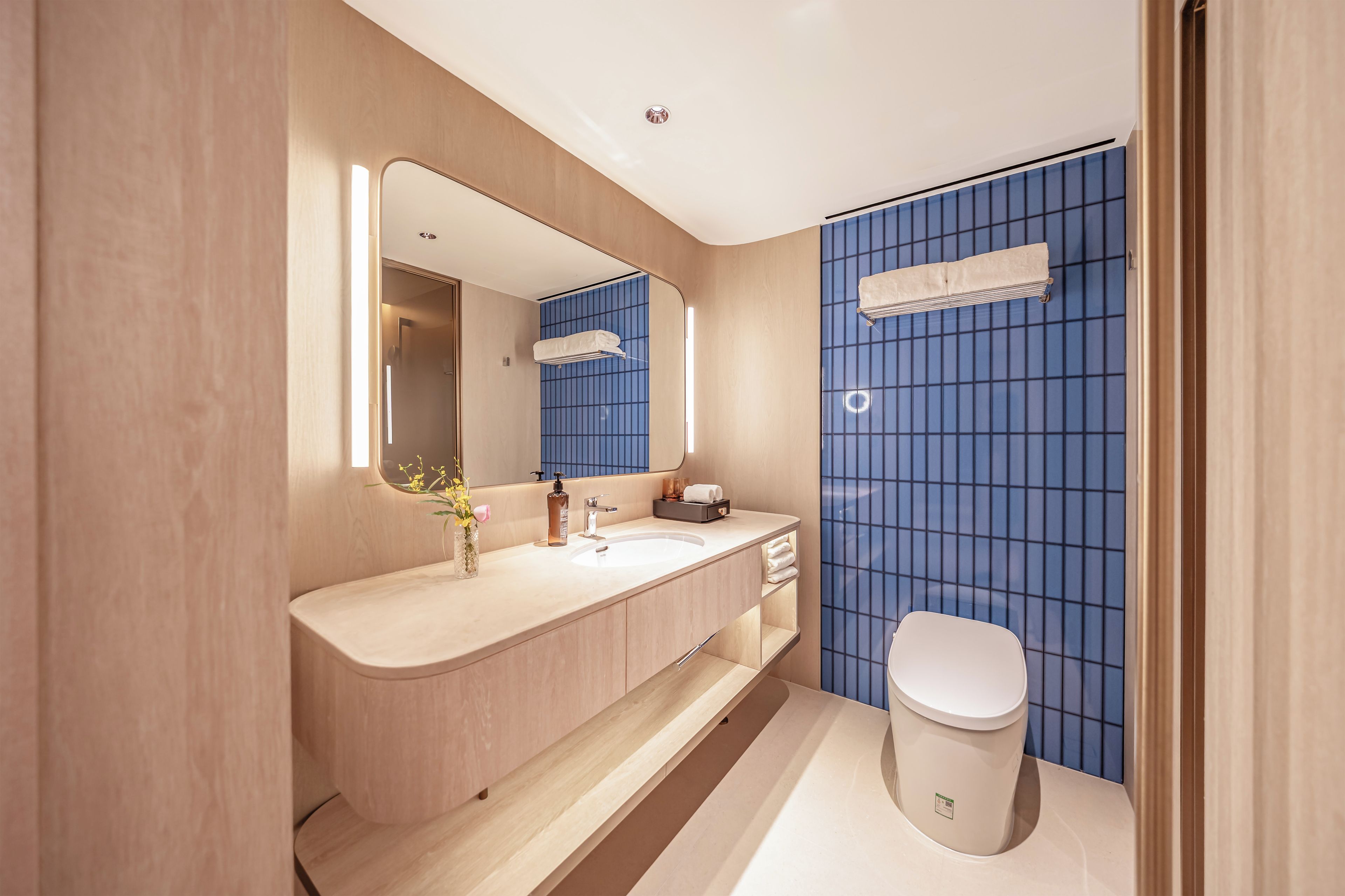 A modern bathroom with a wooden vanity, a large mirror, a sink, and a toilet.