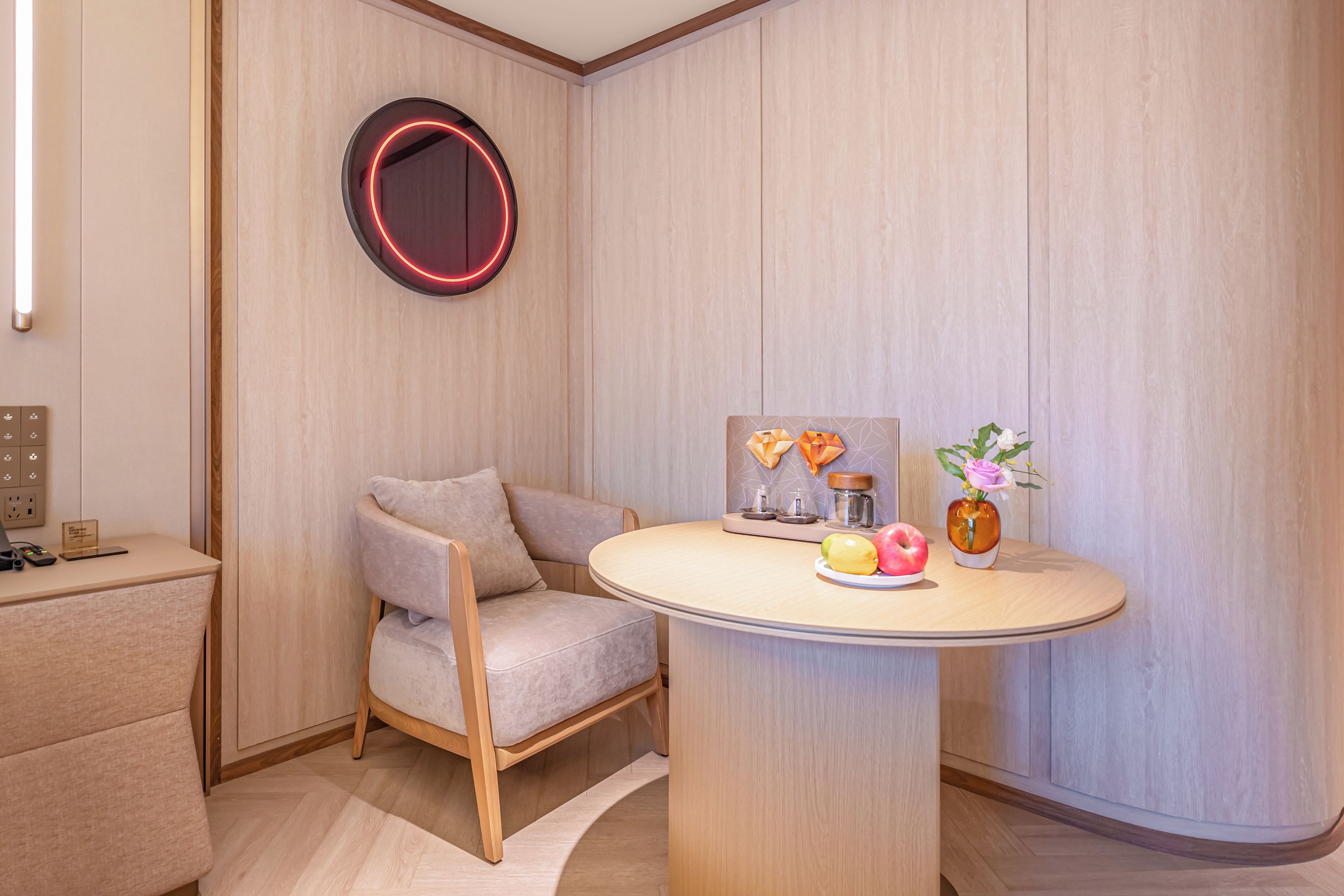 A modern room with a round table, a chair, a wall-mounted mirror, and a small painting.
