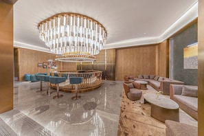 A modern lobby with a central bar, seating area, and a large chandelier.