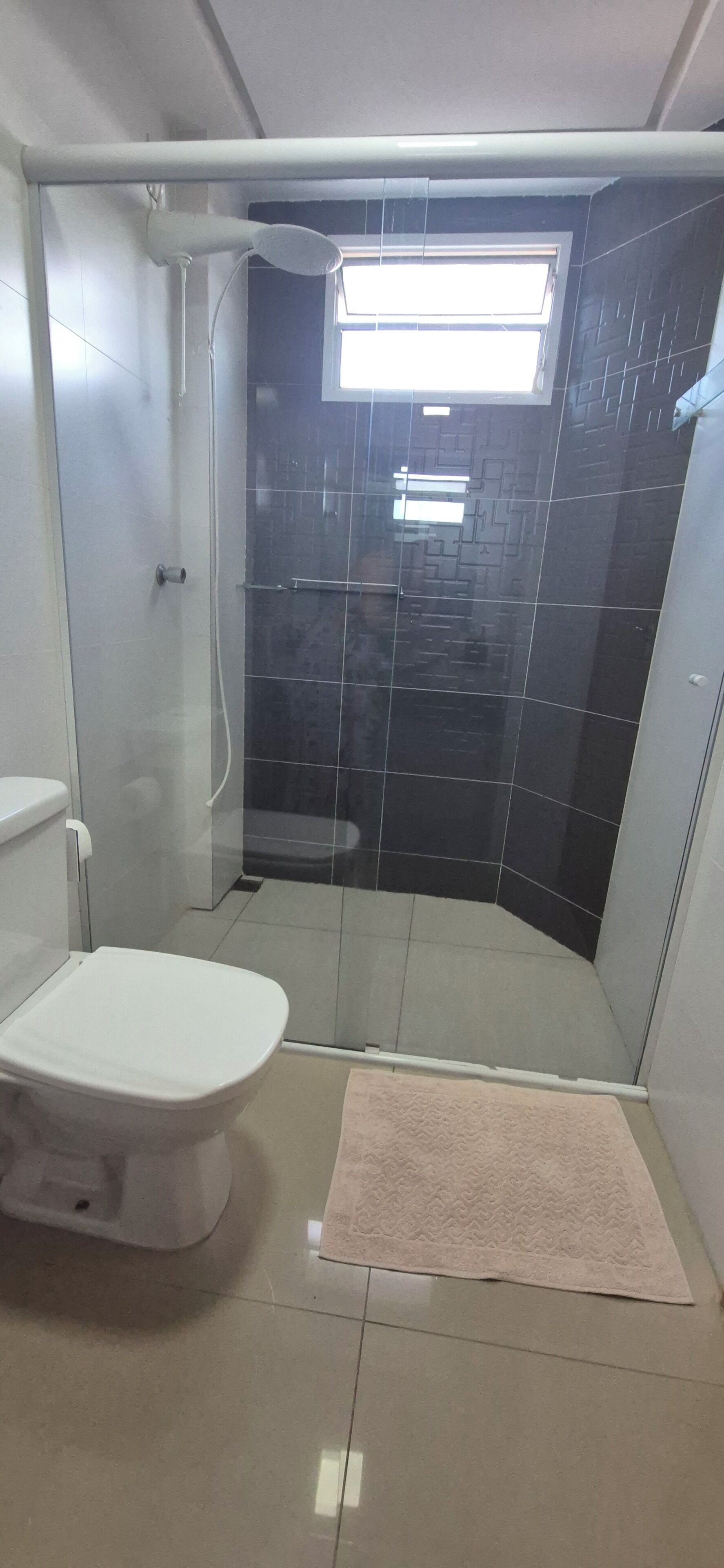 A bathroom with a toilet, a shower enclosure, and a small rug.