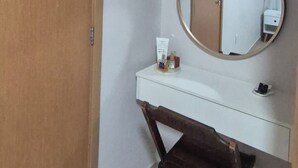 A room with a wooden door, a white vanity with a mirror, and a small stool.