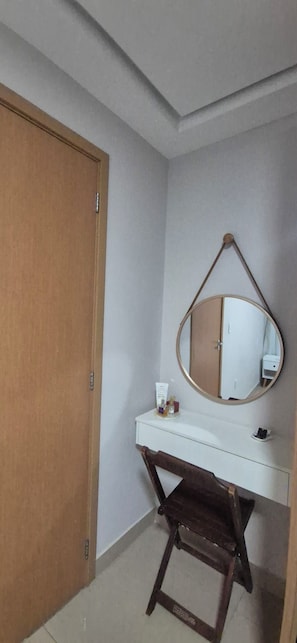 A room with a wooden door, a white vanity with a mirror, and a small stool.