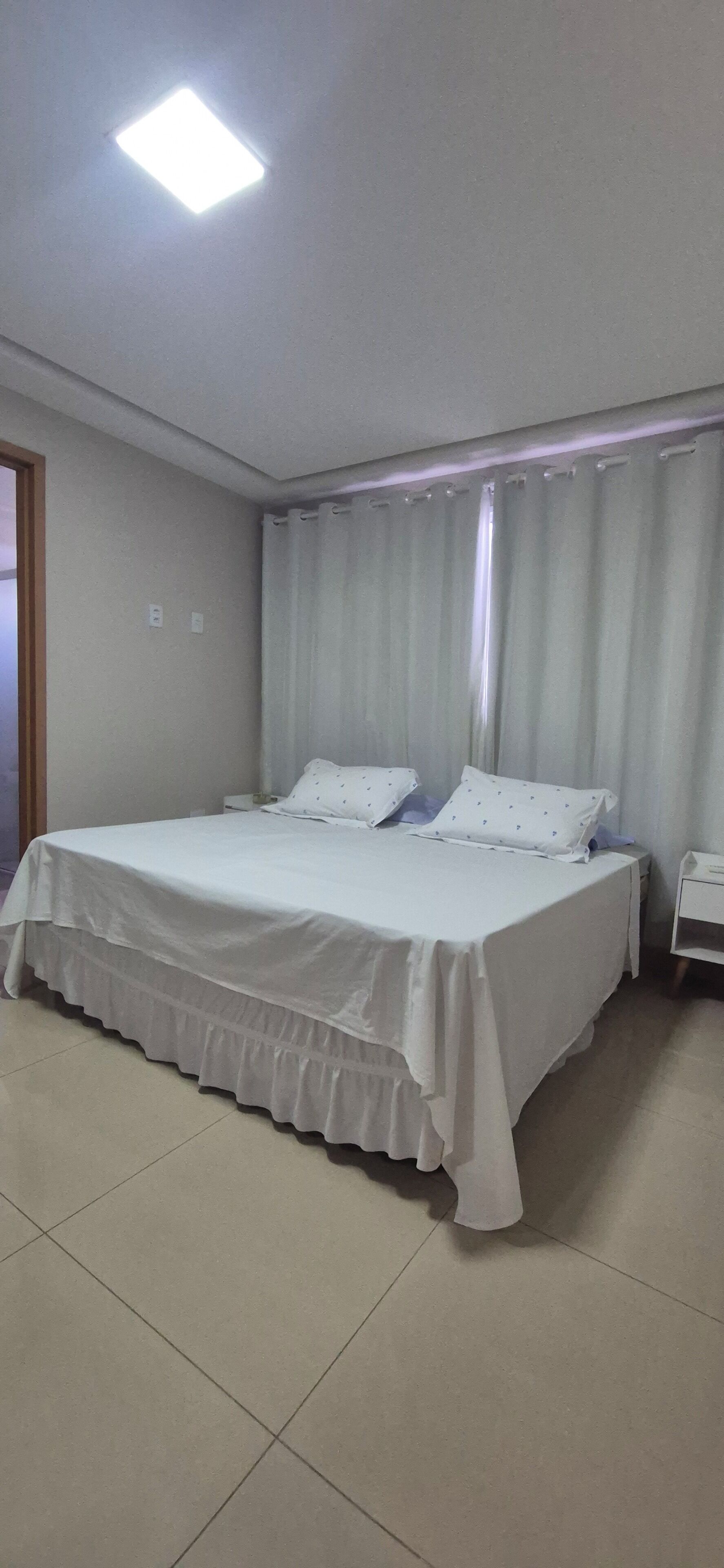 Habitación de hotel estándar con una cama individual, una mesita de noche y un ventanal con cortinas.