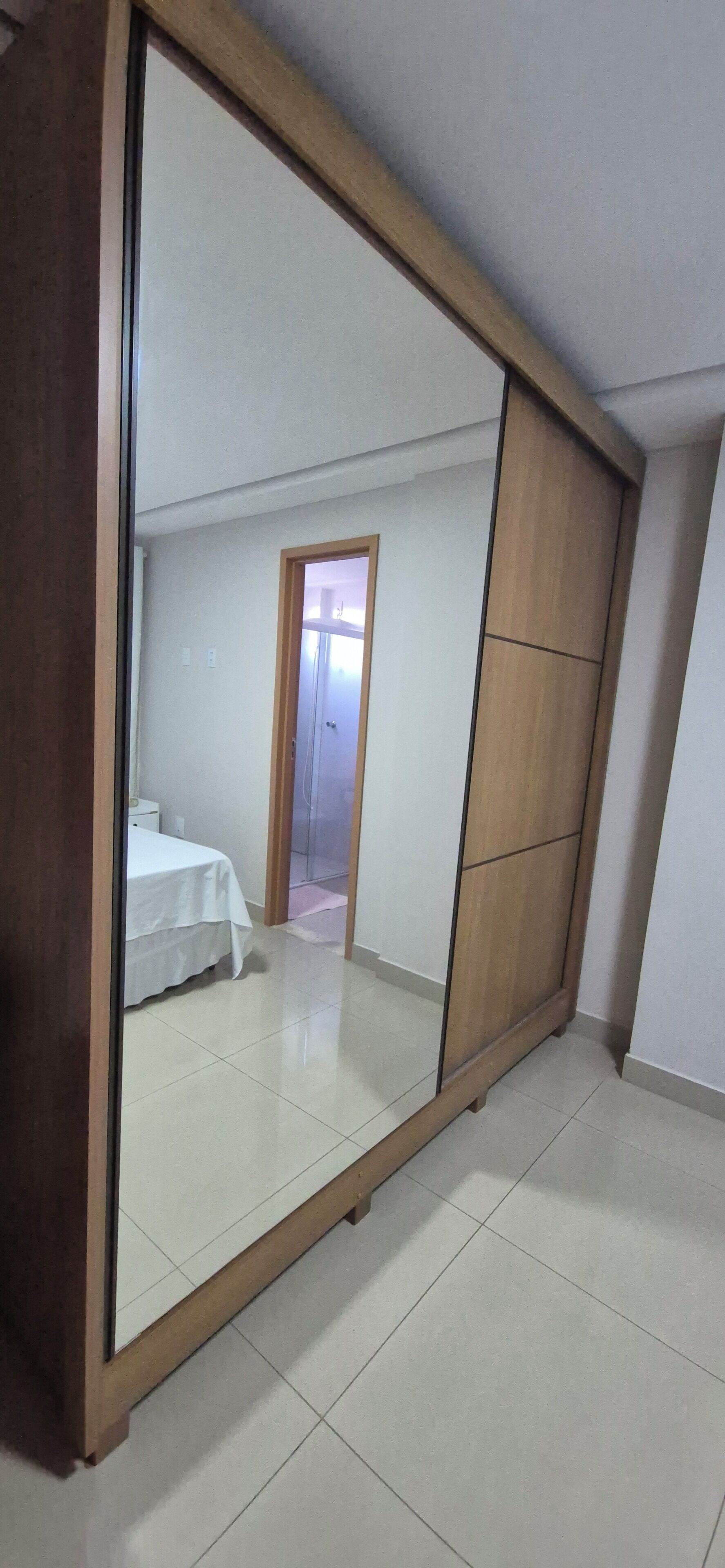 A room with a large mirror, a bed, and a door leading to a bathroom.