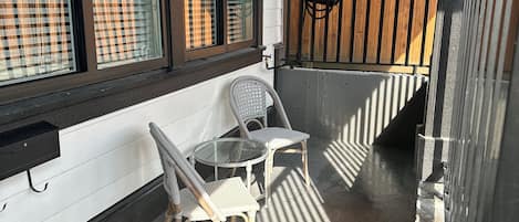 Un espace extérieur abrité, aménagé avec une table et deux chaises, une clôture en bois en arrière-plan et une fenêtre avec des stores.