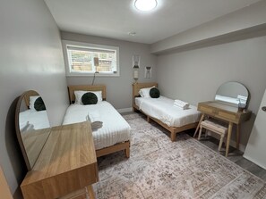 A bedroom with two beds, a wooden dresser, a mirror, and a patterned rug.