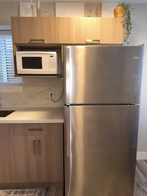 A kitchen with a stainless steel refrigerator, a microwave, wooden cabinets, and a marble countertop.