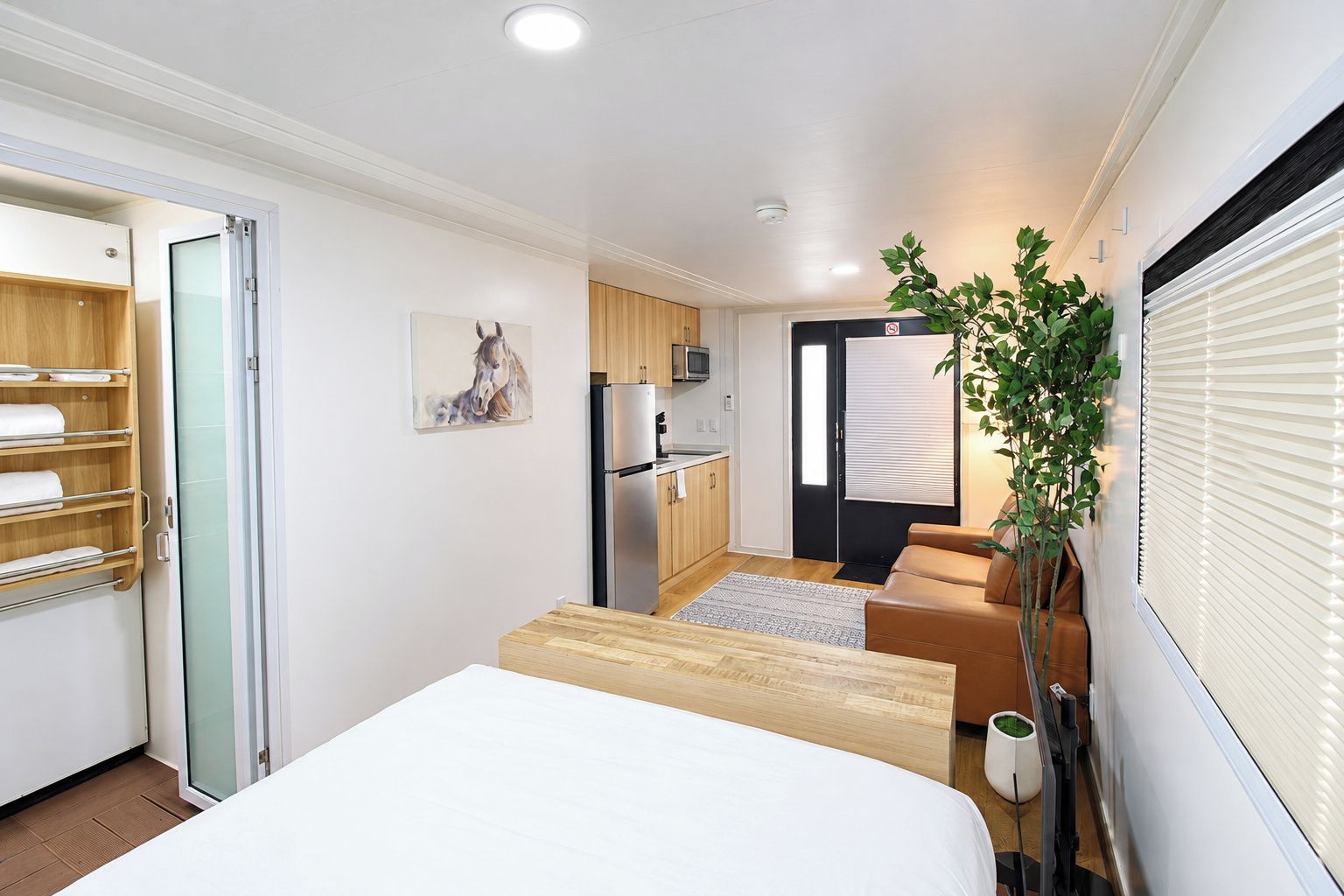 A compact hotel room with a bed, a small kitchenette, a seating area, and a door leading to a balcony.