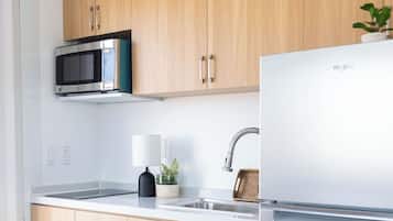 A modern kitchen with wooden cabinets, a stainless steel microwave, a white refrigerator, and a sink with a faucet.