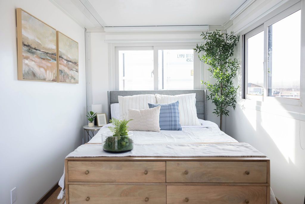 A bedroom with a bed, a nightstand, a potted plant, and a window with a view.