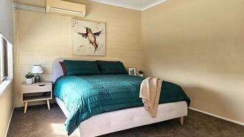 Une chambre à coucher comprenant un lit, une table de chevet, une lampe, un climatiseur mural et un ventilateur de plafond.