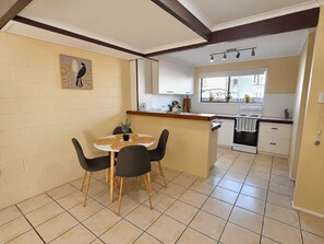 A compact kitchen with a dining area, featuring a white countertop, black chairs, and a tiled floor.