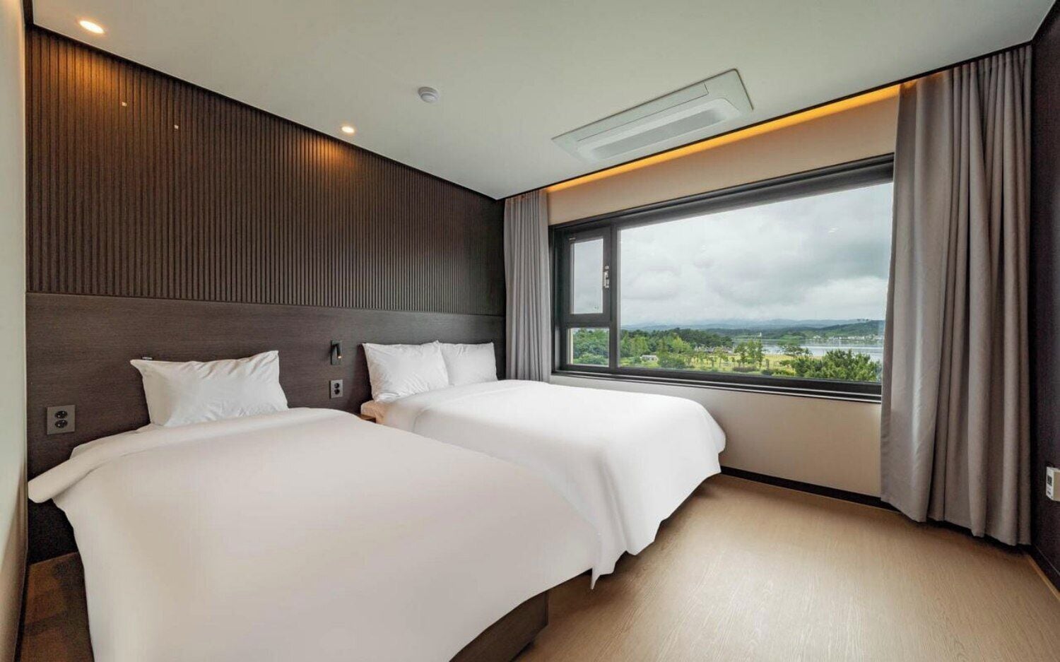 A hotel room with two beds, a large window with a view, and a modern design.