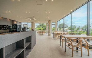 Un café moderno con una barra alargada, mesas de madera y amplios ventanales que dan a zonas verdes.