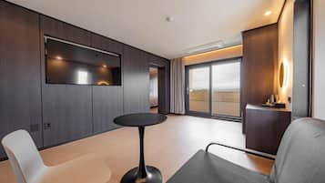A modern hotel room with a large window, a round table, and a seating area.