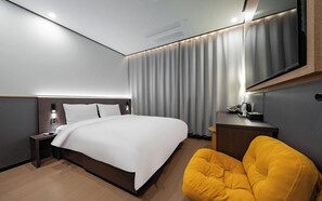 Ein modernes Hotelzimmer mit einem großen Bett, einem Nachttisch, einem Sessel, einem Schreibtisch und einem Spiegel.