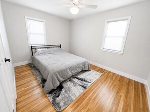 Ein Schlafzimmer mit einem Bett, einem Deckenventilator und zwei Fenstern mit Jalousien.
