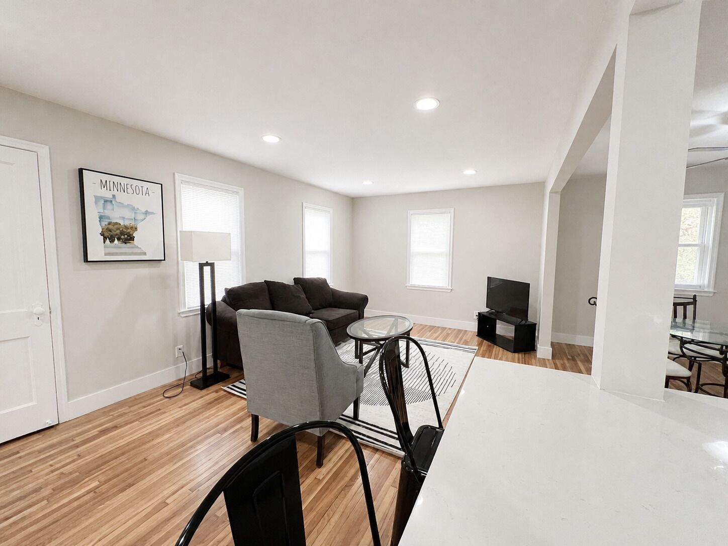A modern living room with a sofa, a glass coffee table, a TV, and a dining area with a table and chairs.