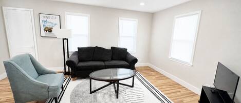 A living room with a sofa, armchair, coffee table, and a flat-screen TV.