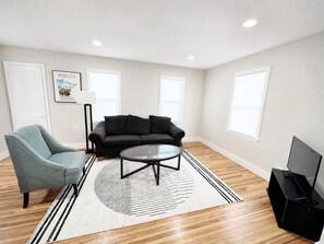 Ein Wohnzimmer mit Sofa, Sessel, Couchtisch und Flachbildfernseher.