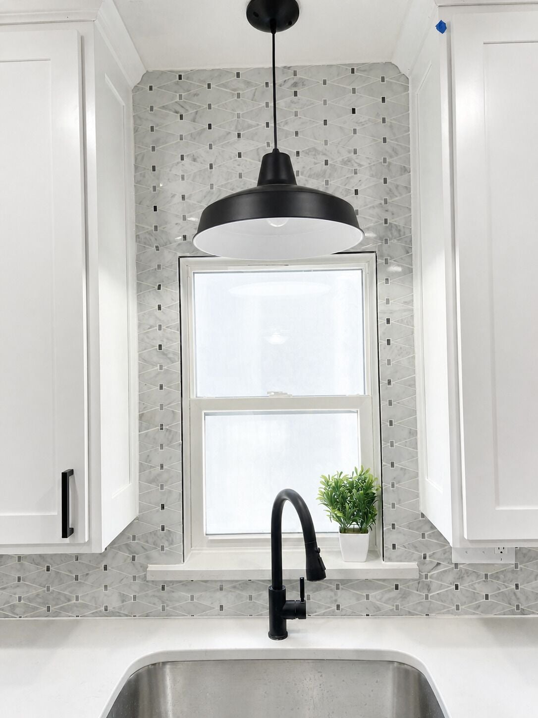 A kitchen with a modern design, featuring a black pendant light, a window with a view, and a sink with a faucet.
