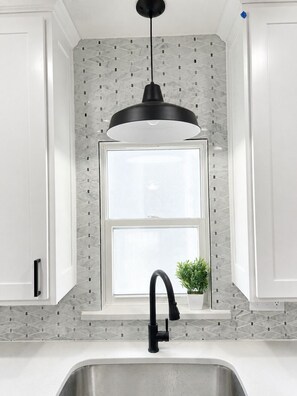 Una cucina dal design moderno, con una lampada a sospensione nera, una finestra vista e un lavello con rubinetto.