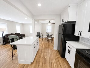 A modern kitchen with white cabinetry, a black refrigerator, and a stove. There is a dining area with a table and chairs. - Kutzky Duplex: Modern 2BR Near Mayo with Free Parking (Rochester)