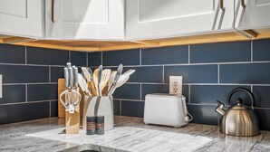 A kitchen with white cabinets, a marble countertop, a toaster, a kettle, and a utensil holder.