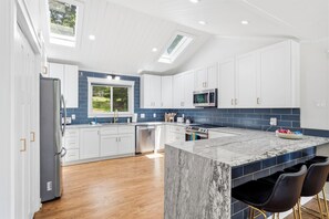 Una cocina moderna con gabinetes blancos, una isla de mármol y un tragaluz.