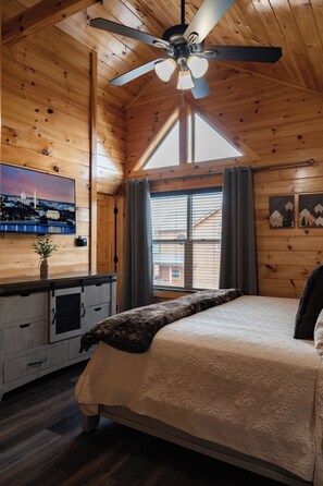 A bedroom with a bed, a ceiling fan, a window with curtains, a television, and a wooden dresser. - Heated Indoor Pool + Hot Tub + Game Room Near Parkway (Pigeon Forge)