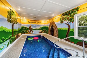 An indoor swimming pool with a mural depicting a landscape and a bear, surrounded by walls with a yellow and green color scheme. - Heated Indoor Pool + Hot Tub + Game Room Near Parkway (Pigeon Forge)