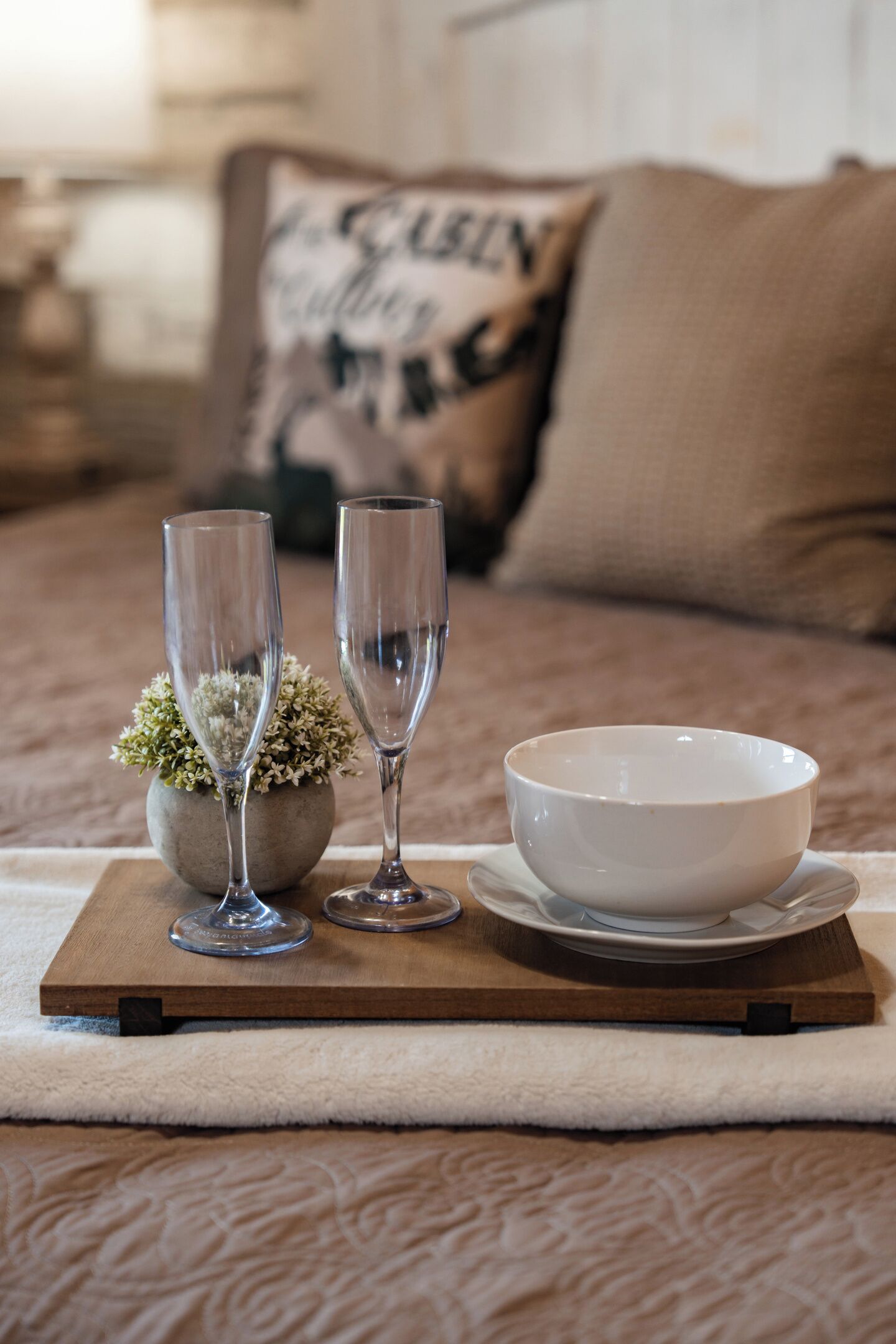 A wooden tray with two clear glasses and a white bowl on a textured fabric surface.