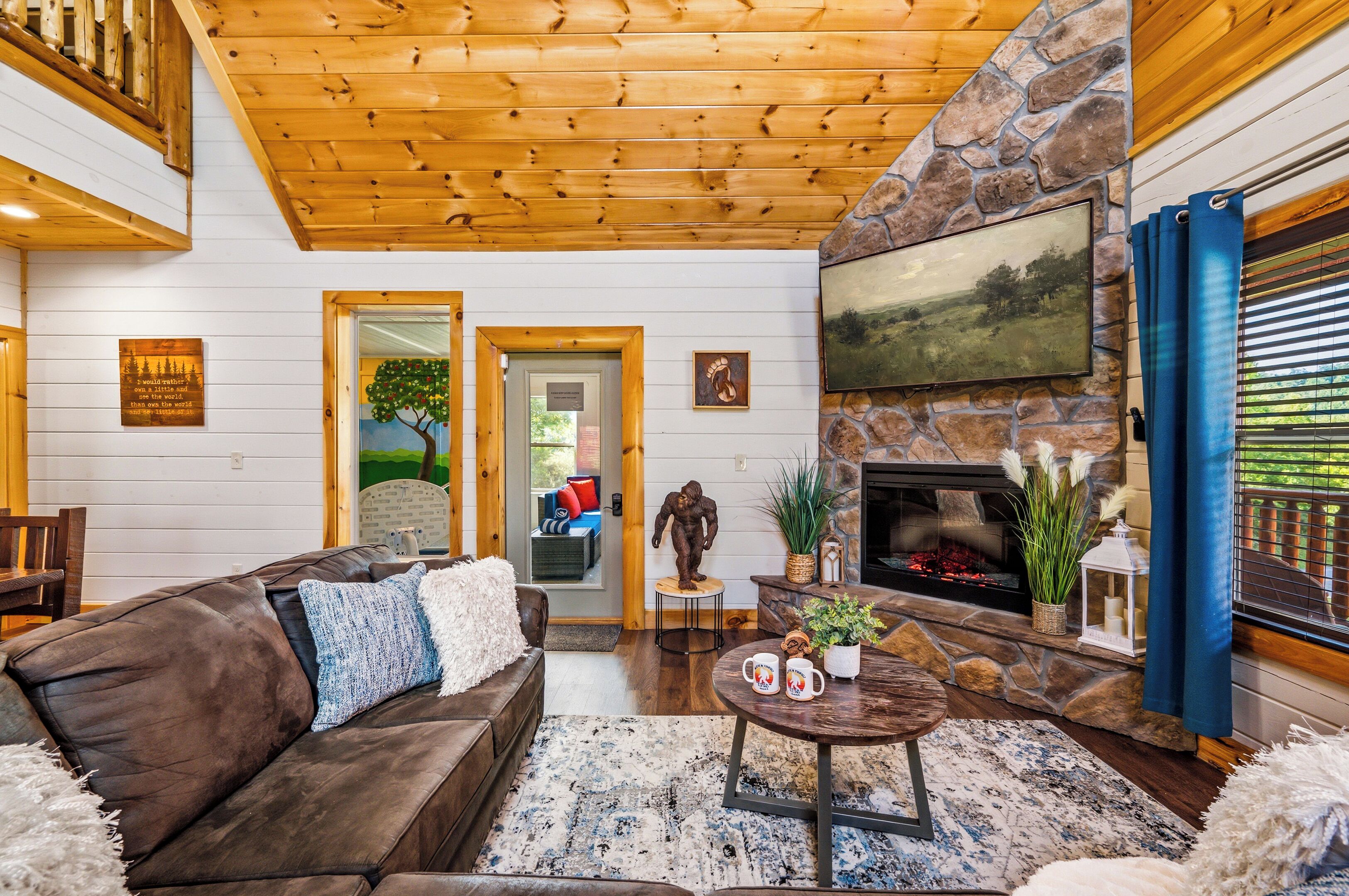 A cozy living room with a stone fireplace, a large painting, and a wooden ceiling.