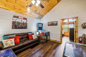 A cozy room with a leather sofa, wooden walls, and a ceiling fan. - Heated Indoor Pool + Hot Tub + Game Room Near Parkway (Pigeon Forge)