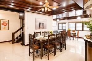 A dining area with a wooden table and chairs, a ceiling fan, and a large window with blinds. - 4-Bedroom House in Chang Khlan Chiang Mai (Chang Wat Chiang Mai)