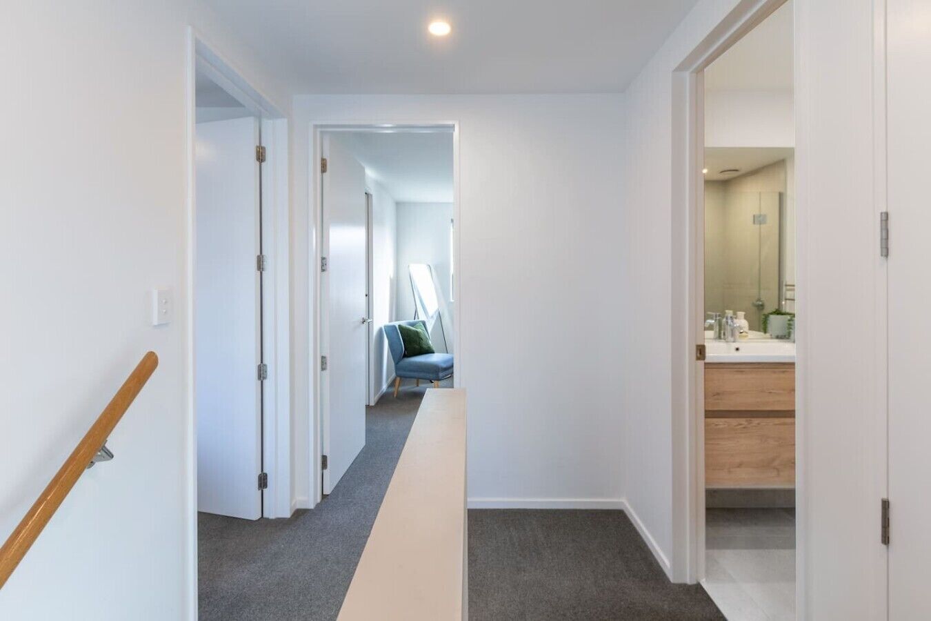 A hallway with a wooden handrail, carpeted floor, and a view into a room with a bathroom.