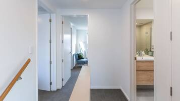 A hallway with a wooden handrail, carpeted floor, and a view into a room with a bathroom.