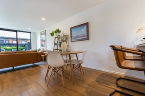 A modern living room with a sofa, dining table, chairs, and a view of the outside. - Spacious St Albans Stay – Near CBD, Garage + BBQ (Christchurch)