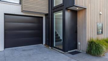 A modern two-story house with a dark garage door, a glass entrance, and a small outdoor area with a planter.