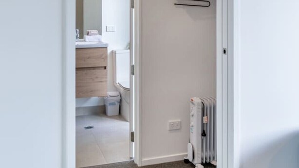 Ein Flur, der zu einem Badezimmer mit weißem Heizkörper und einer Kleiderstange führt.