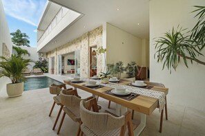 Uma área de refeições moderna com vista para a piscina, paredes de pedra e plantas dentro de casa.