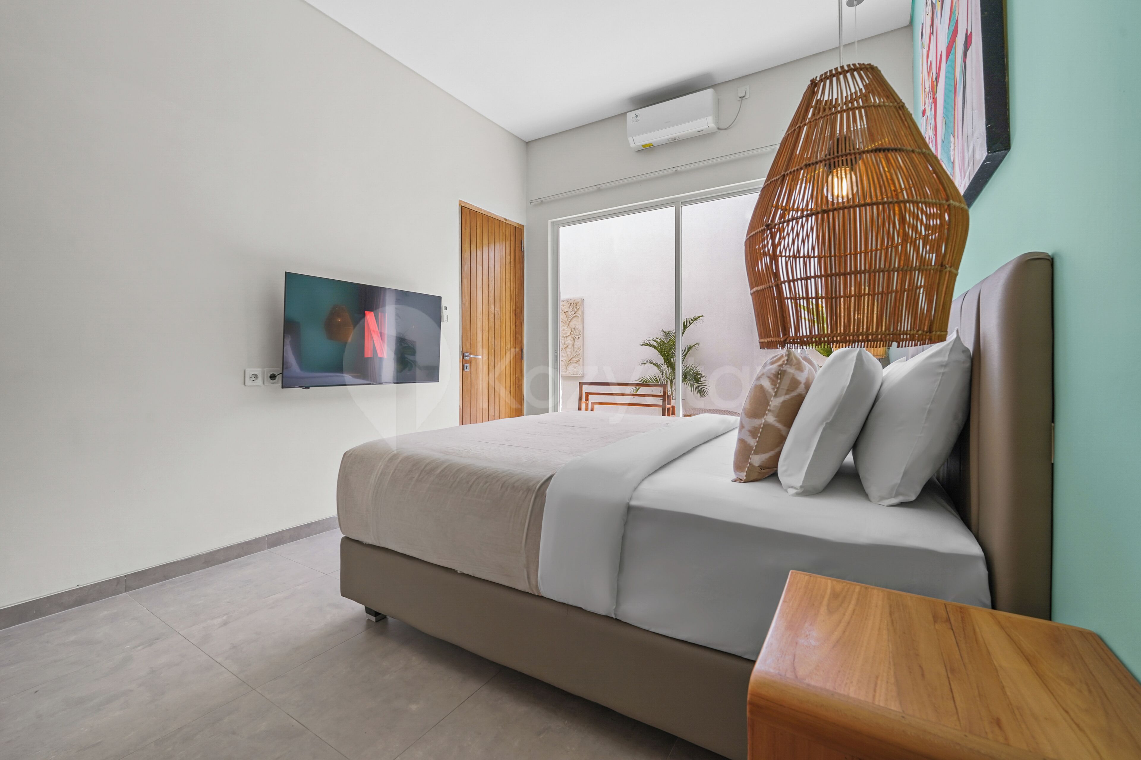 Un dormitorio moderno con una cama grande, un televisor en la pared y una lámpara de mimbre.