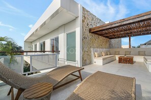 Een moderne buitenruimte met rieten meubilair, een stenen muur en een houten pergola.