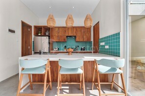 A modern kitchen with wooden cabinets, a white countertop, and three light blue chairs. - Arkapura Villa by Kozystay - Canggu (Badung)