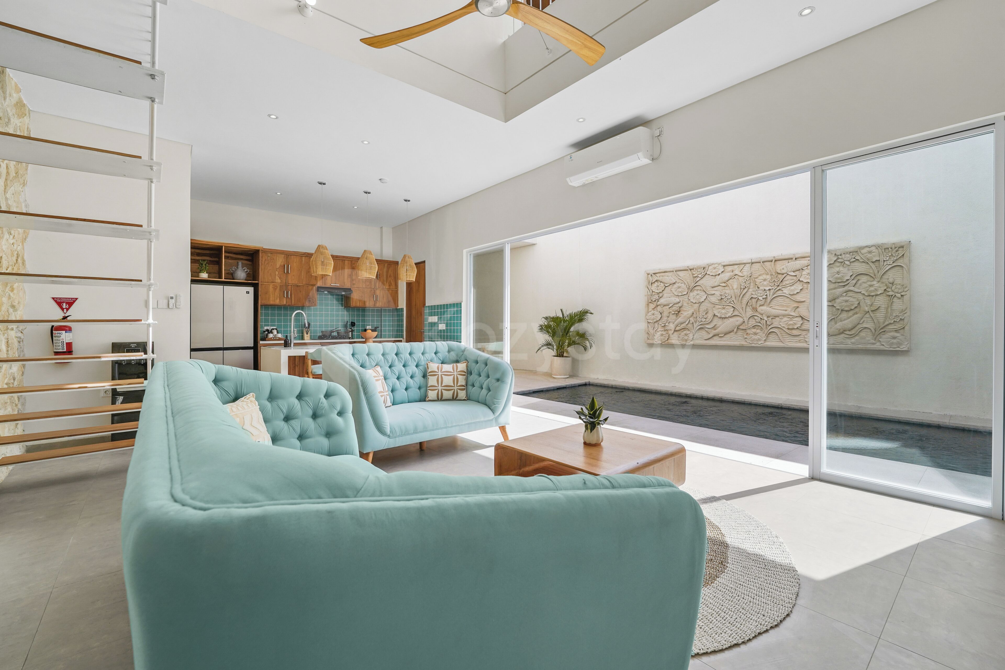 A modern living room with a sofa, coffee table, and a view of a kitchen and outdoor area.