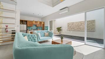 A modern living room with a sofa, coffee table, and a view of a kitchen and outdoor area.